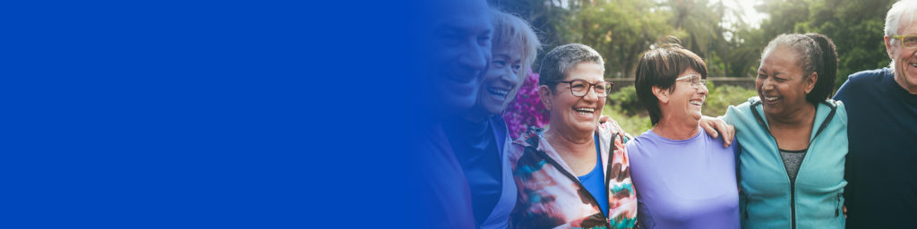 A group of five older adults stand outdoors smiling and laughing together, with greenery in the background and a blue gradient on the left side of the image.